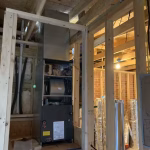 HVAC technician performing a new heating system replacement and furnace installation in a residential home under construction.