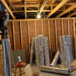 HVAC contractor installing insulated flexible ductwork during a residential basement remodeling project.