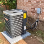 New residential air conditioner condenser unit installed outside a brick home.